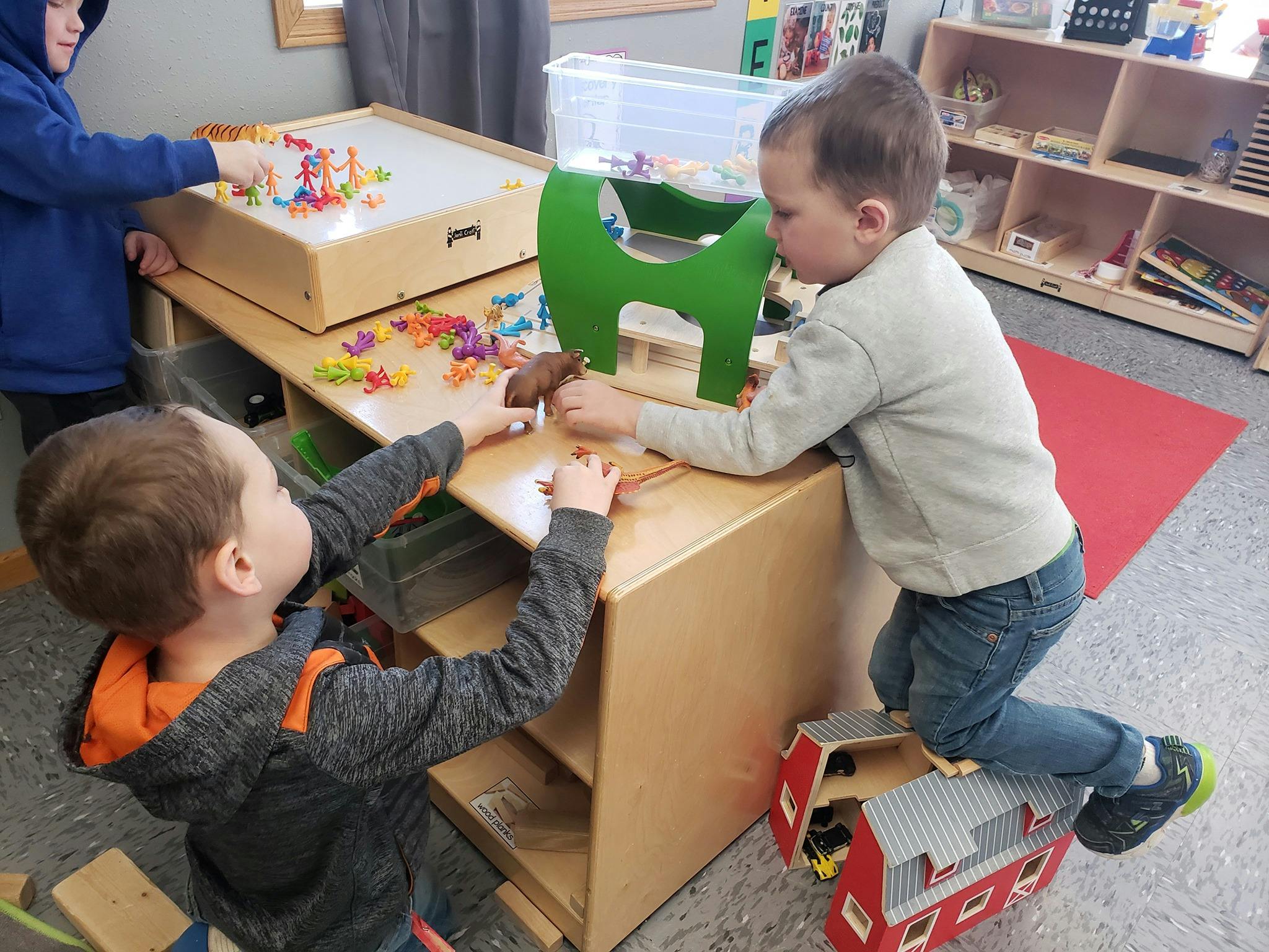 Three children playing with toys at a table in a classroom