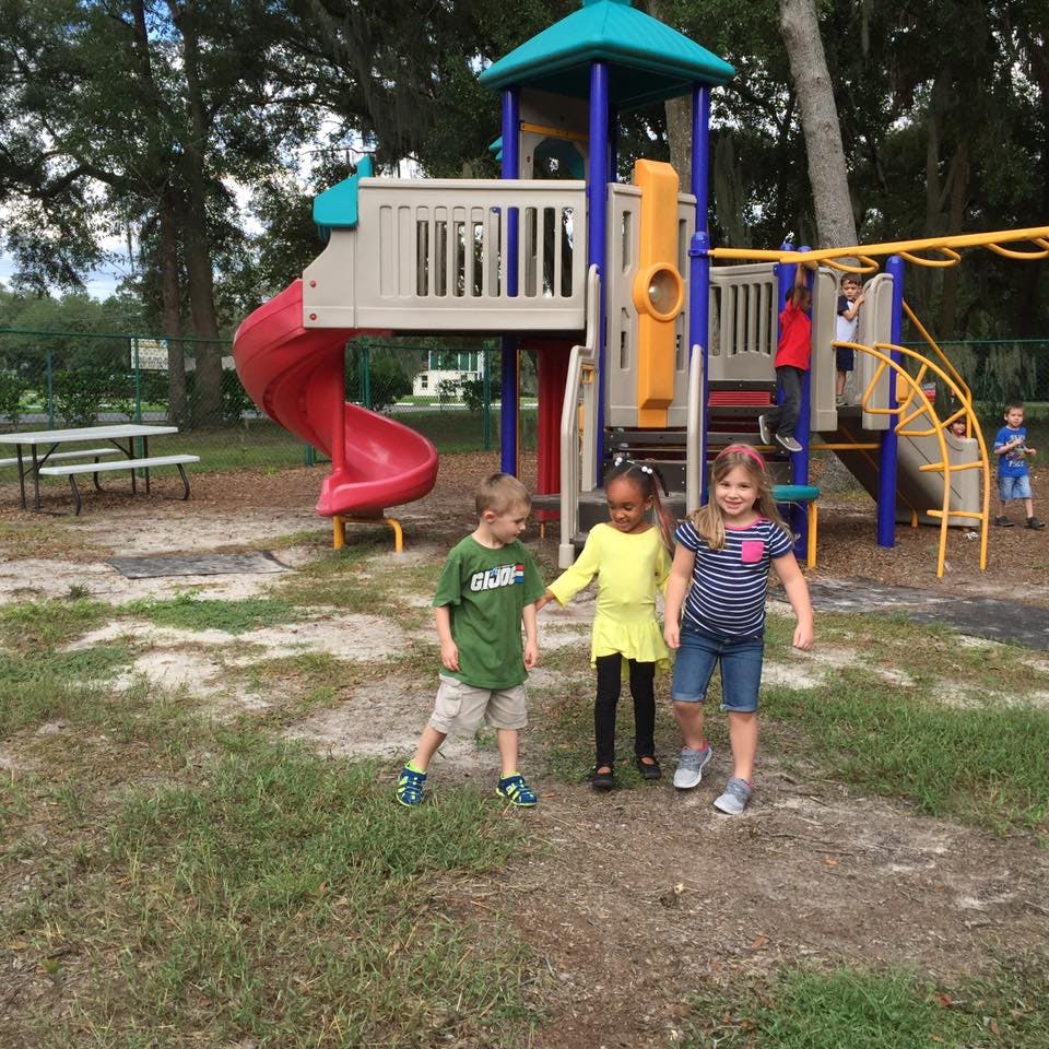 Three children walking on a playground with play structure in background