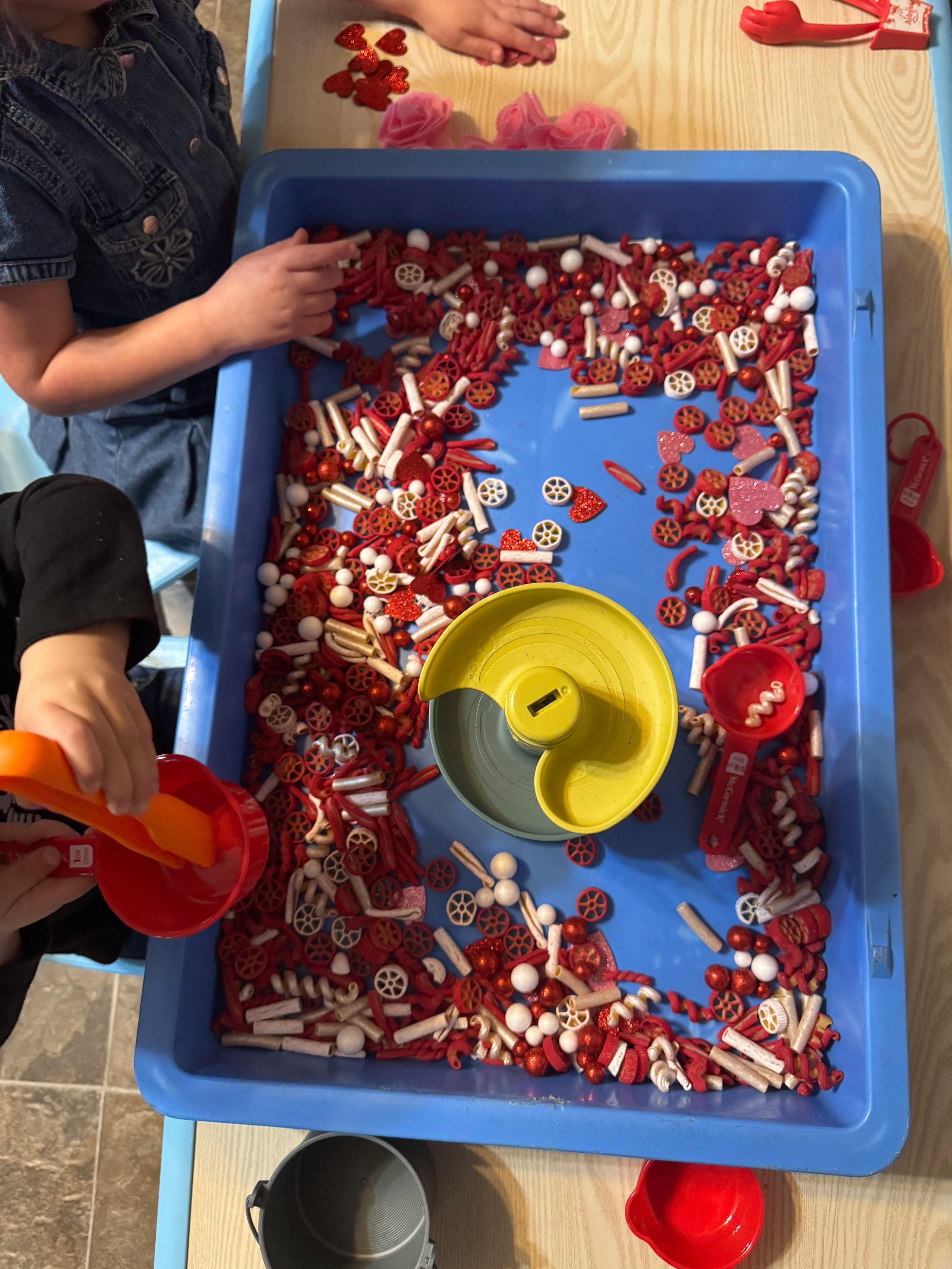 Two children playing with red and white sensory bin fillers in a blue bin