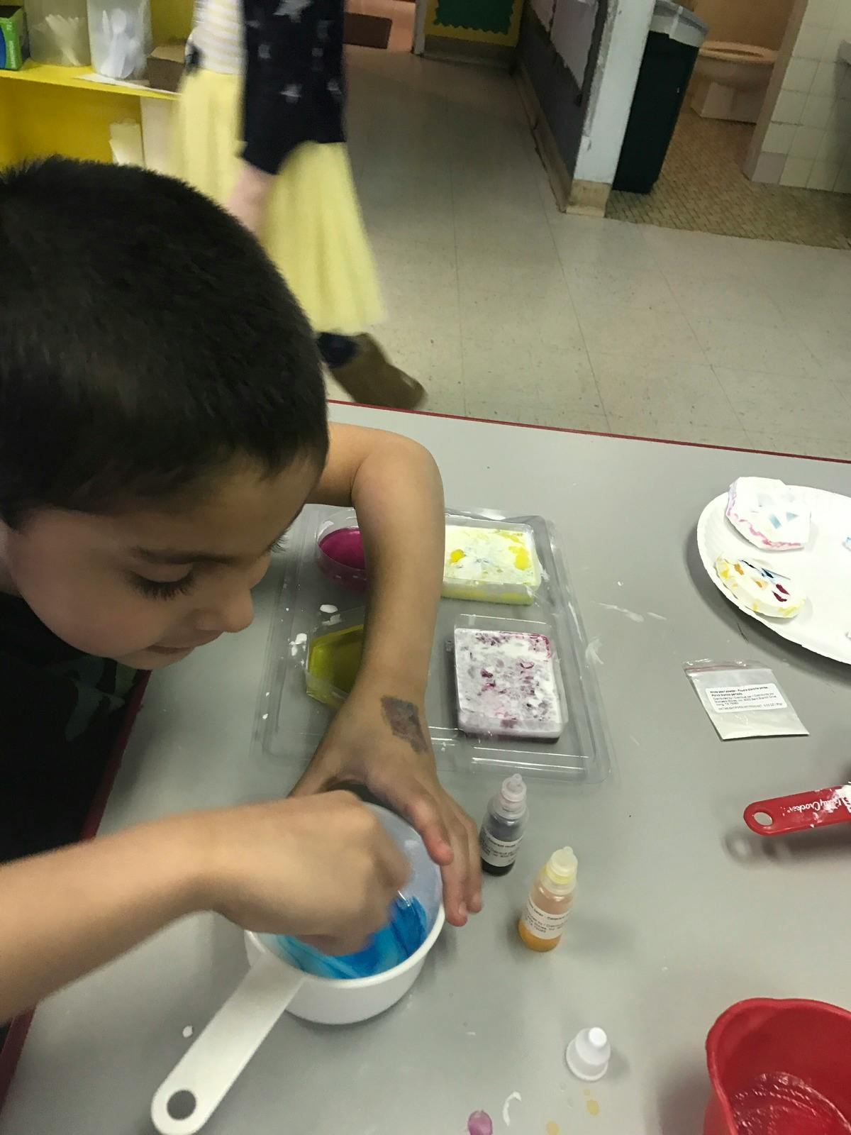 Child mixing blue liquid in a white measuring cup