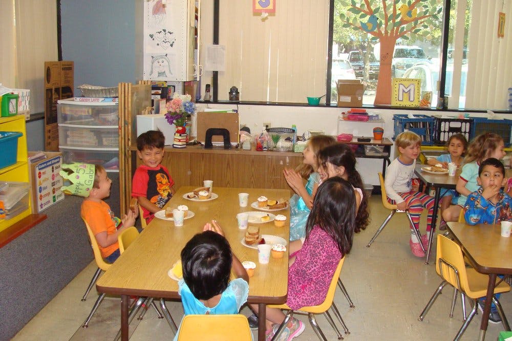 Children sitting at tables in a classroom eating snacks
