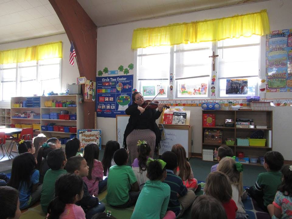 Person playing violin for children in a classroom
