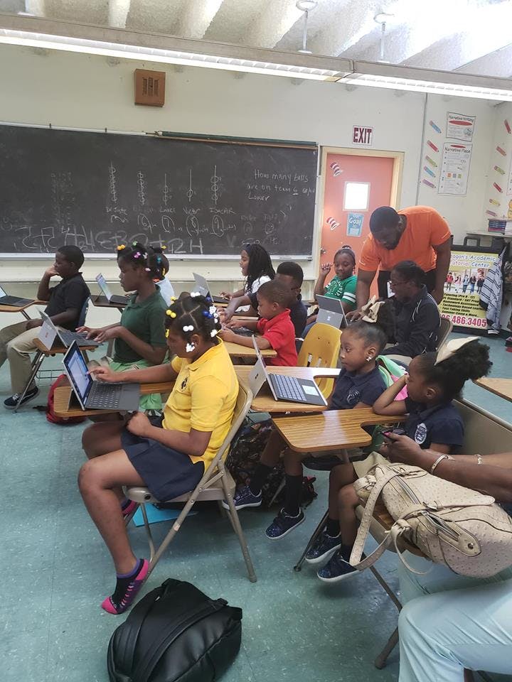 Adult and children in a classroom with laptops