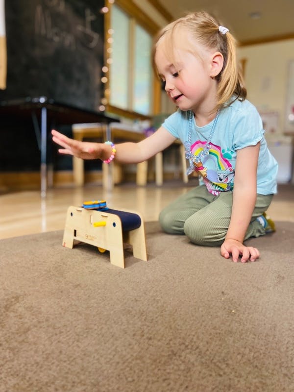 Child kneeling on a rug, reaching for a wooden toy