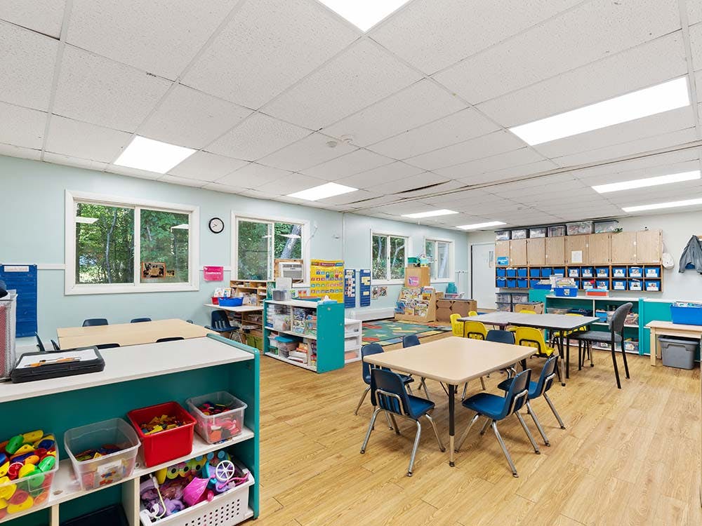 Classroom with small tables and chairs, shelves with toys, and large windows
