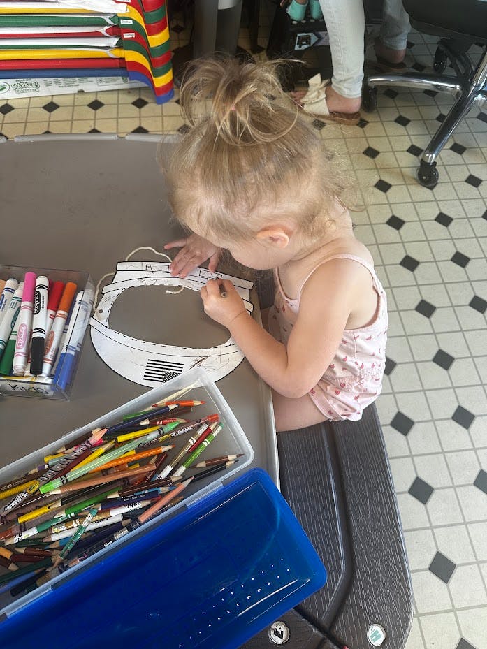 Child coloring a paper astronaut helmet cutout at a table