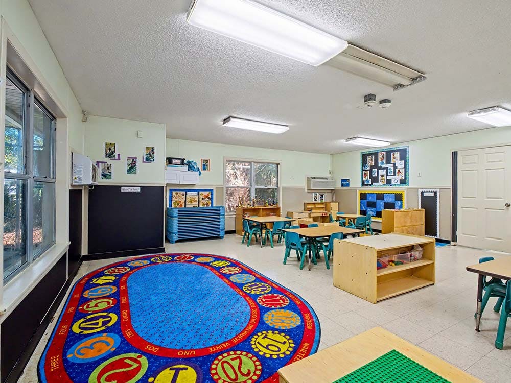 Classroom with small tables and chairs, a large colorful rug, and bulletin boards