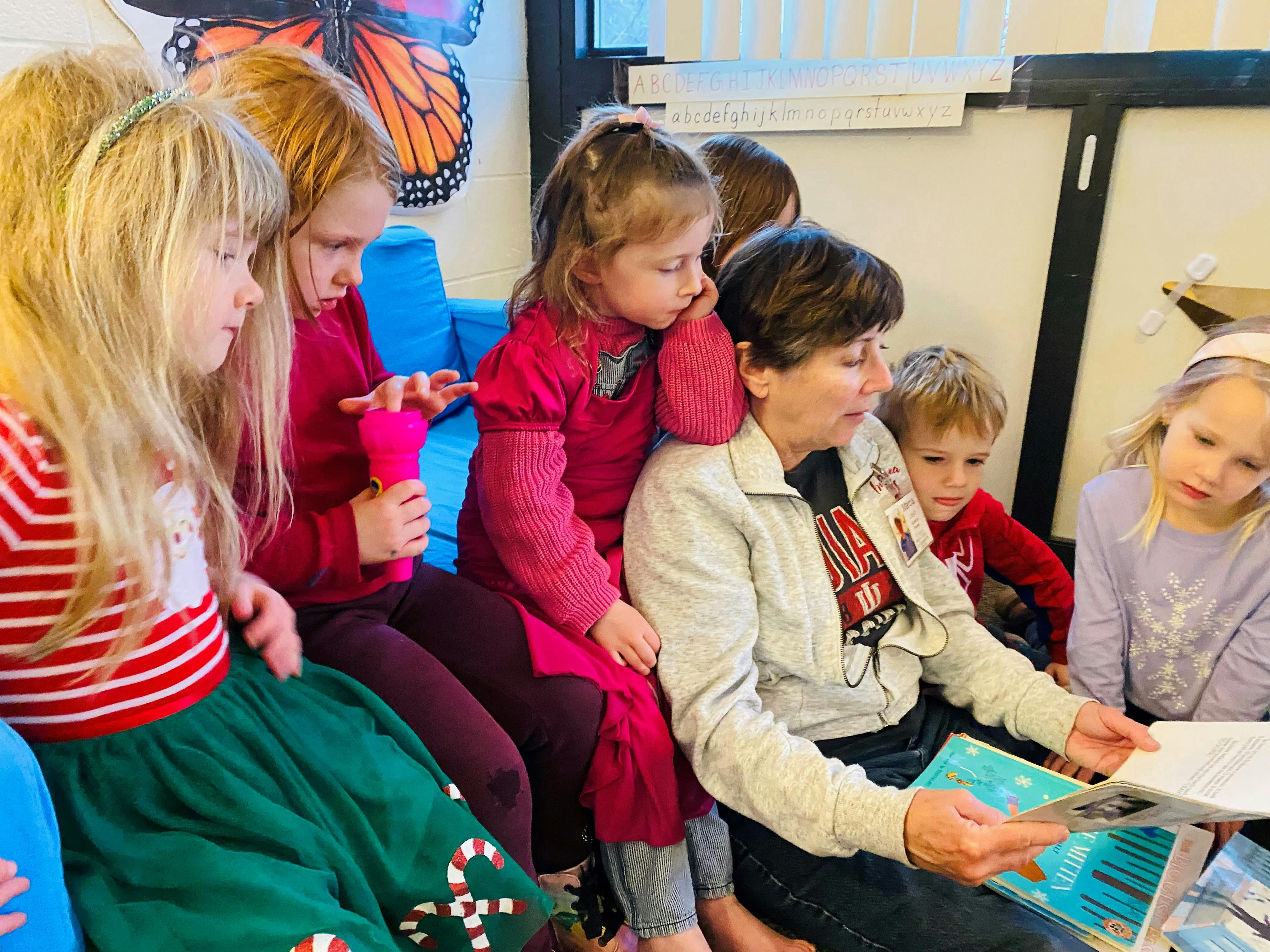 Adult reading a book to a group of children in a classroom