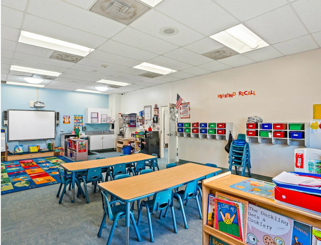 Classroom with small tables and chairs, a whiteboard, and storage shelves