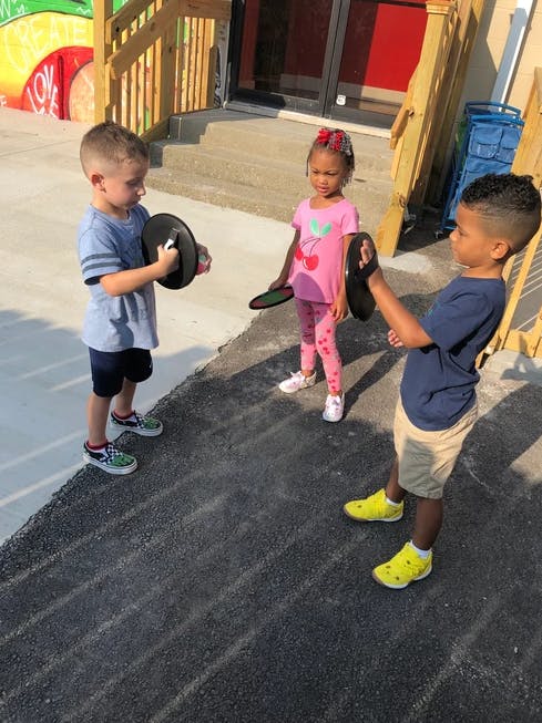 Three children playing with black frisbees outdoors