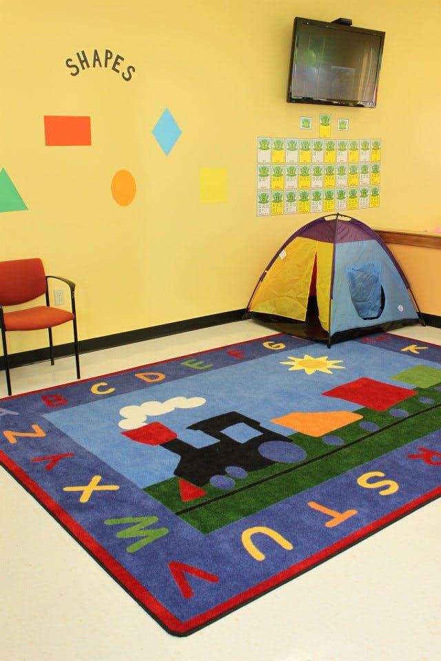 Children's play area with a tent, alphabet rug, and shapes on the wall