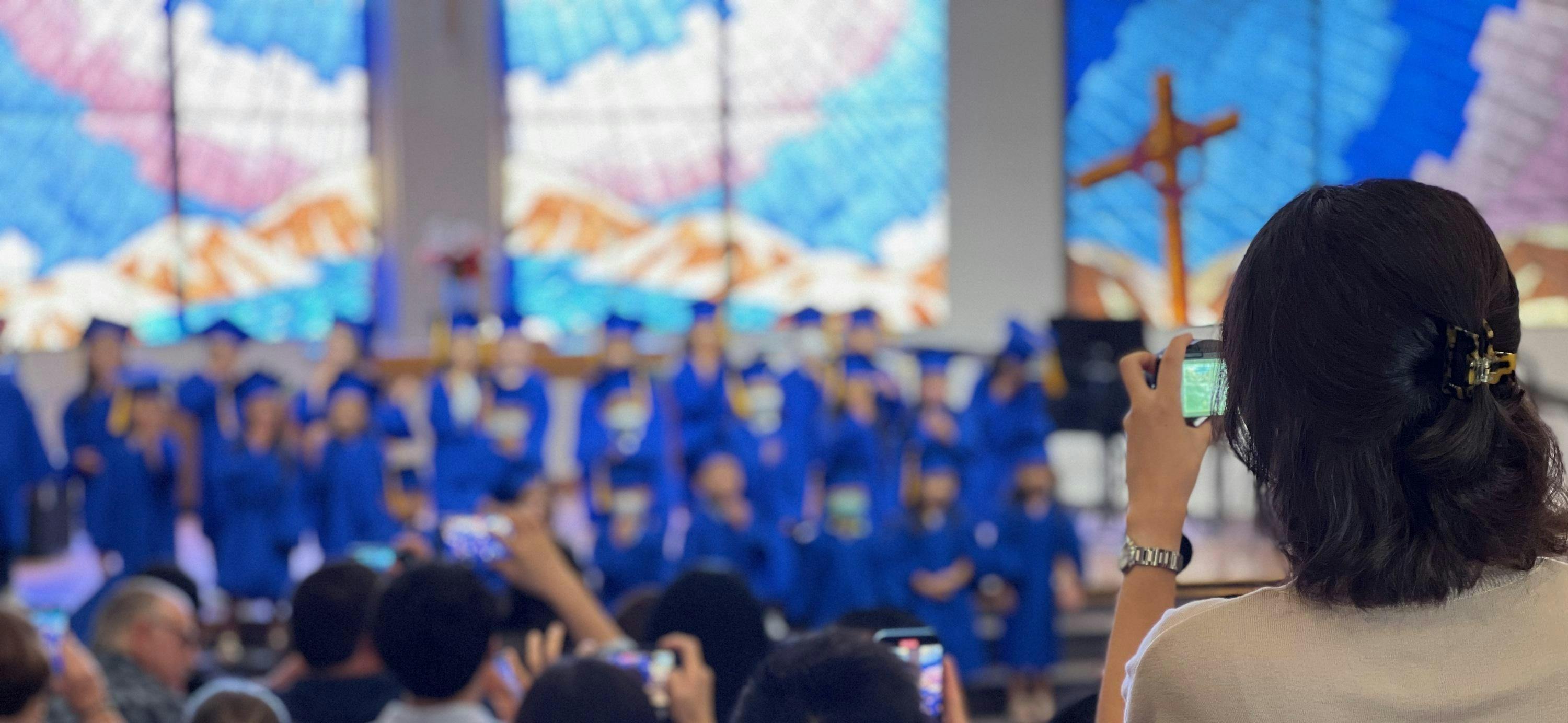 Person taking a photo of people in blue robes on a stage