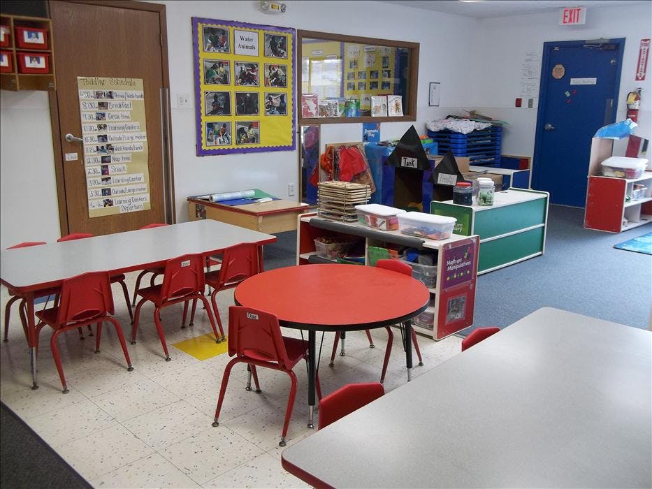 Empty classroom with small tables and chairs, "Toddler Schedule" on the door