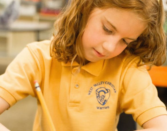 Child in a yellow polo shirt writing with a pencil