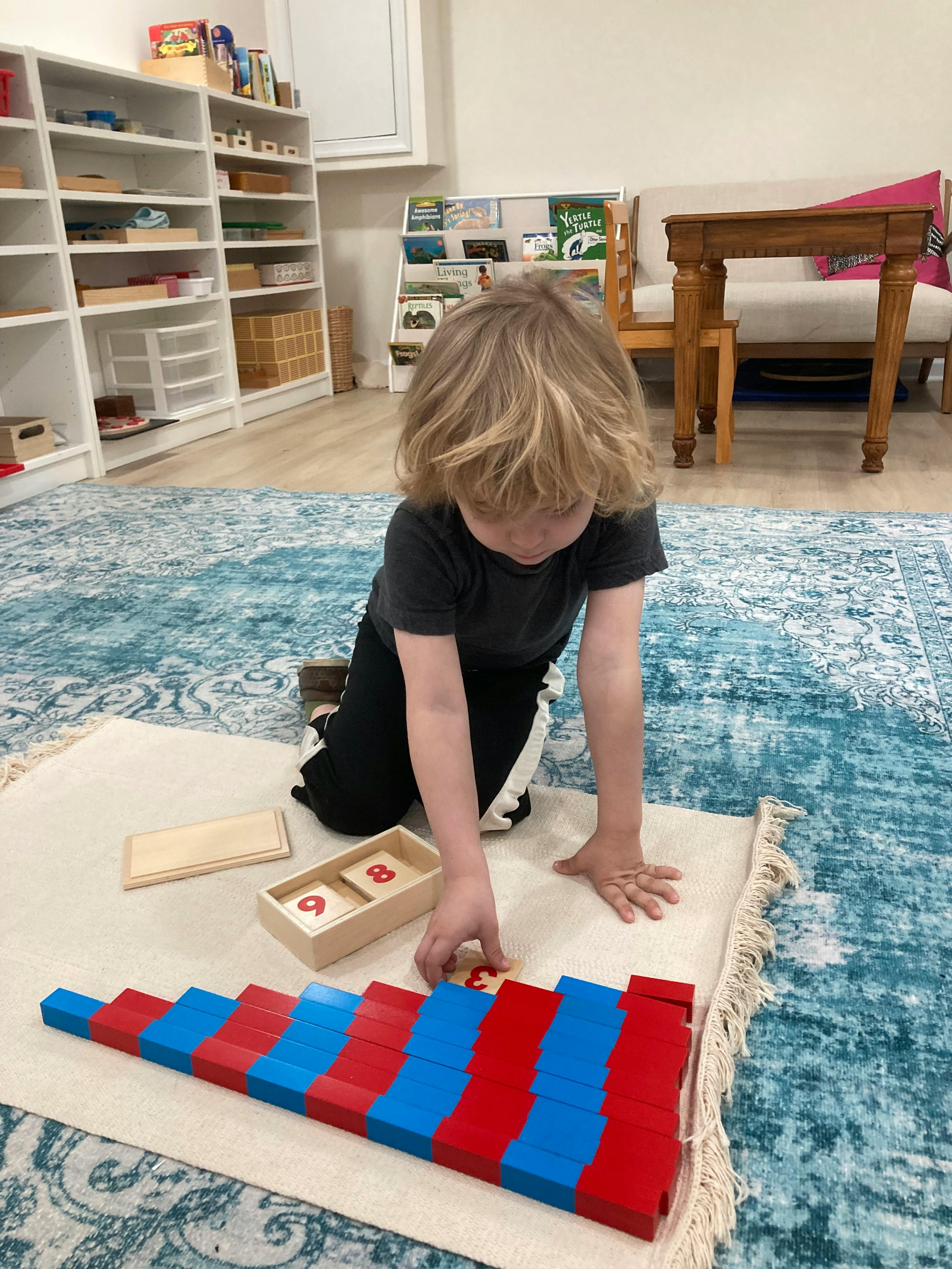 Child kneeling on a rug, playing with red and blue blocks