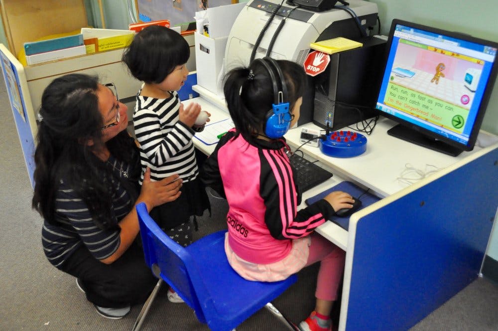 Adult and two children at computer station, one child wearing headphones