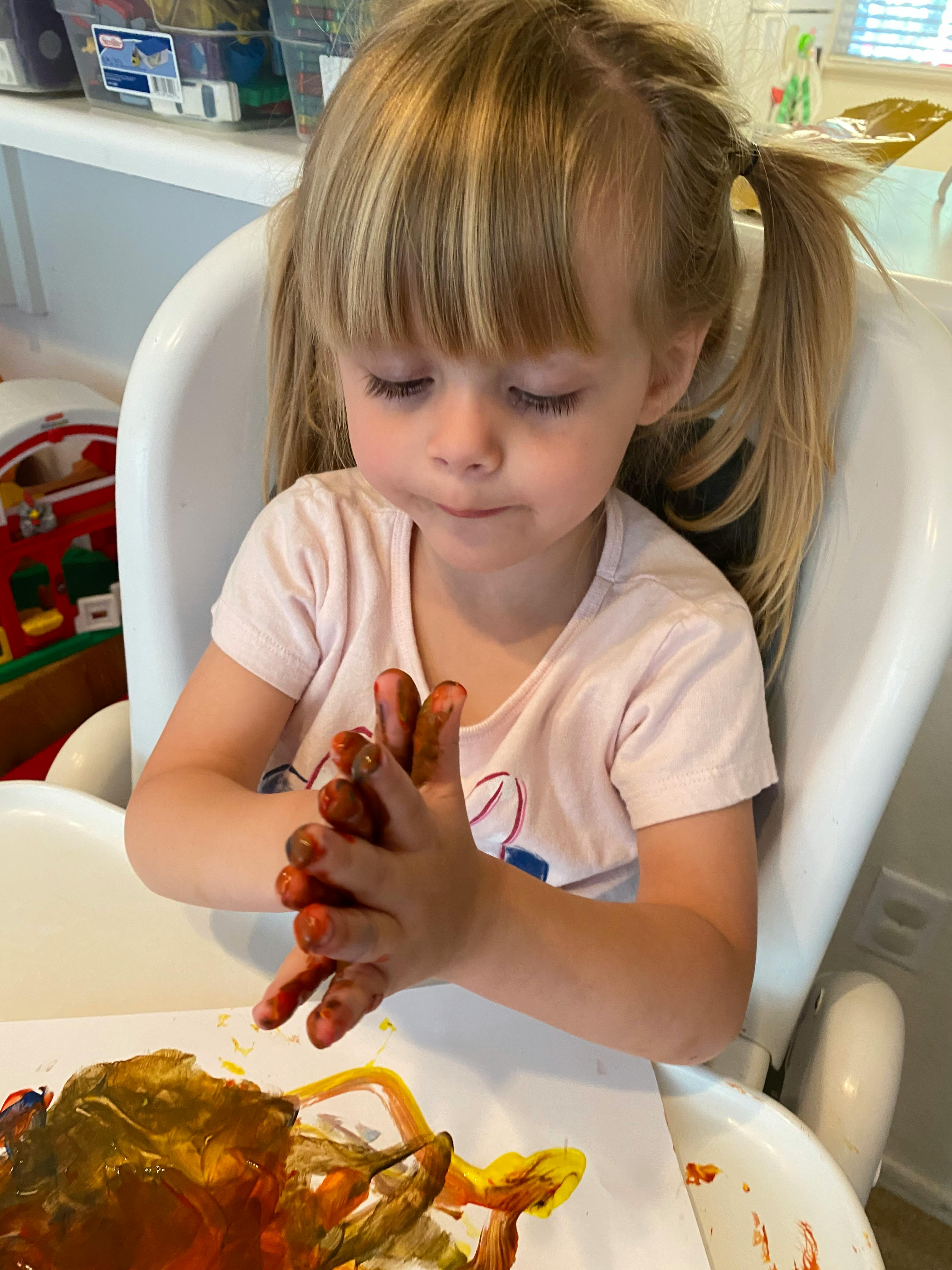 Child with paint on hands over a painting