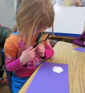 Child looking at paper with a magnifying glass