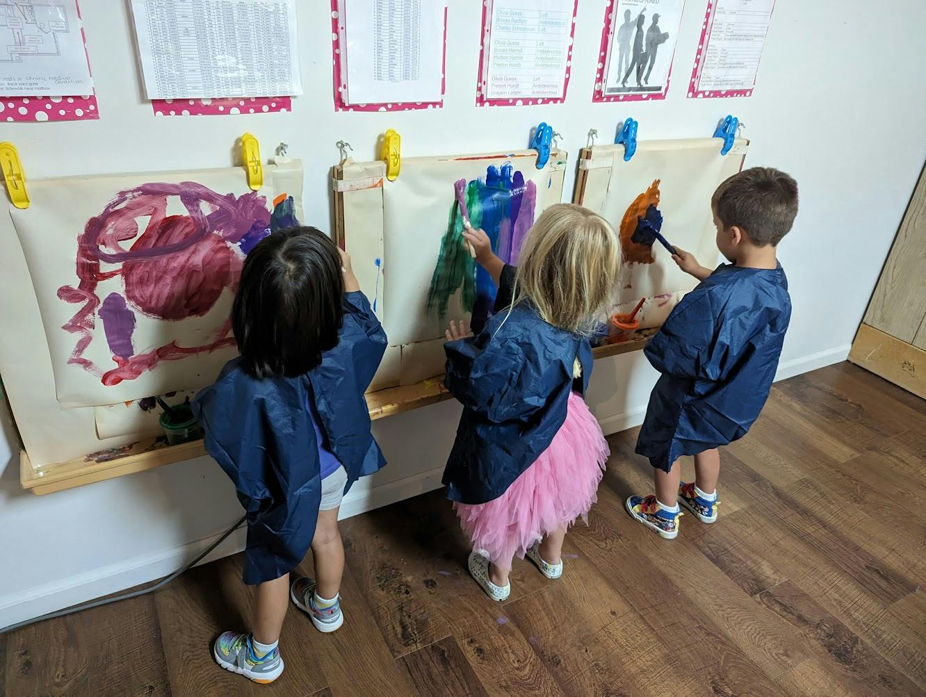 Three children painting on paper in a classroom