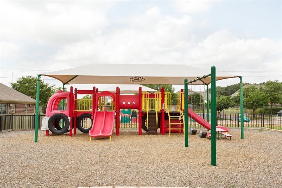 Red and yellow playground structure with slides and climbing areas under a shade