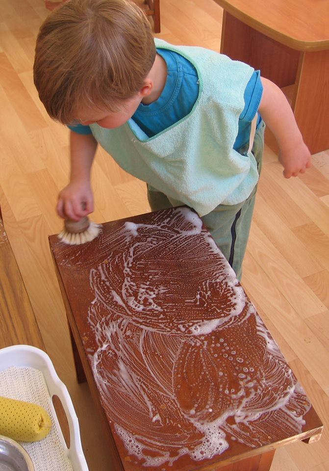 Child scrubbing a wooden surface with a brush and soap suds
