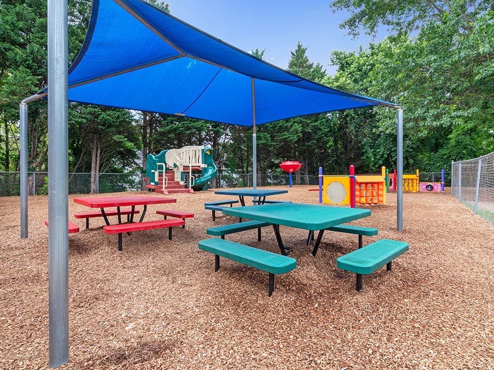 Picnic tables and playground equipment under a blue shade covering