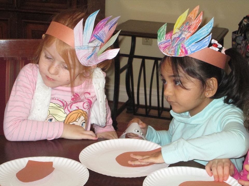 Two children wearing paper feather headbands making crafts at a table