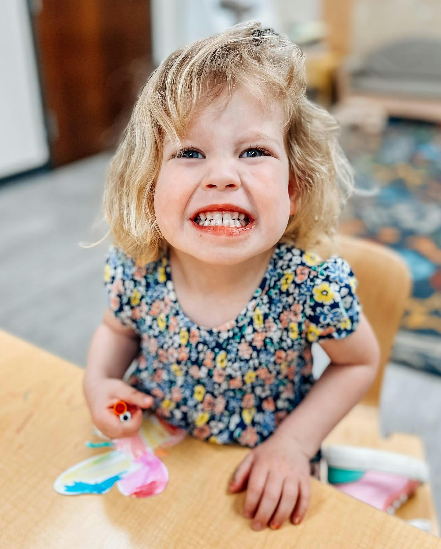 Child with blonde hair smiling, holding a colorful toy