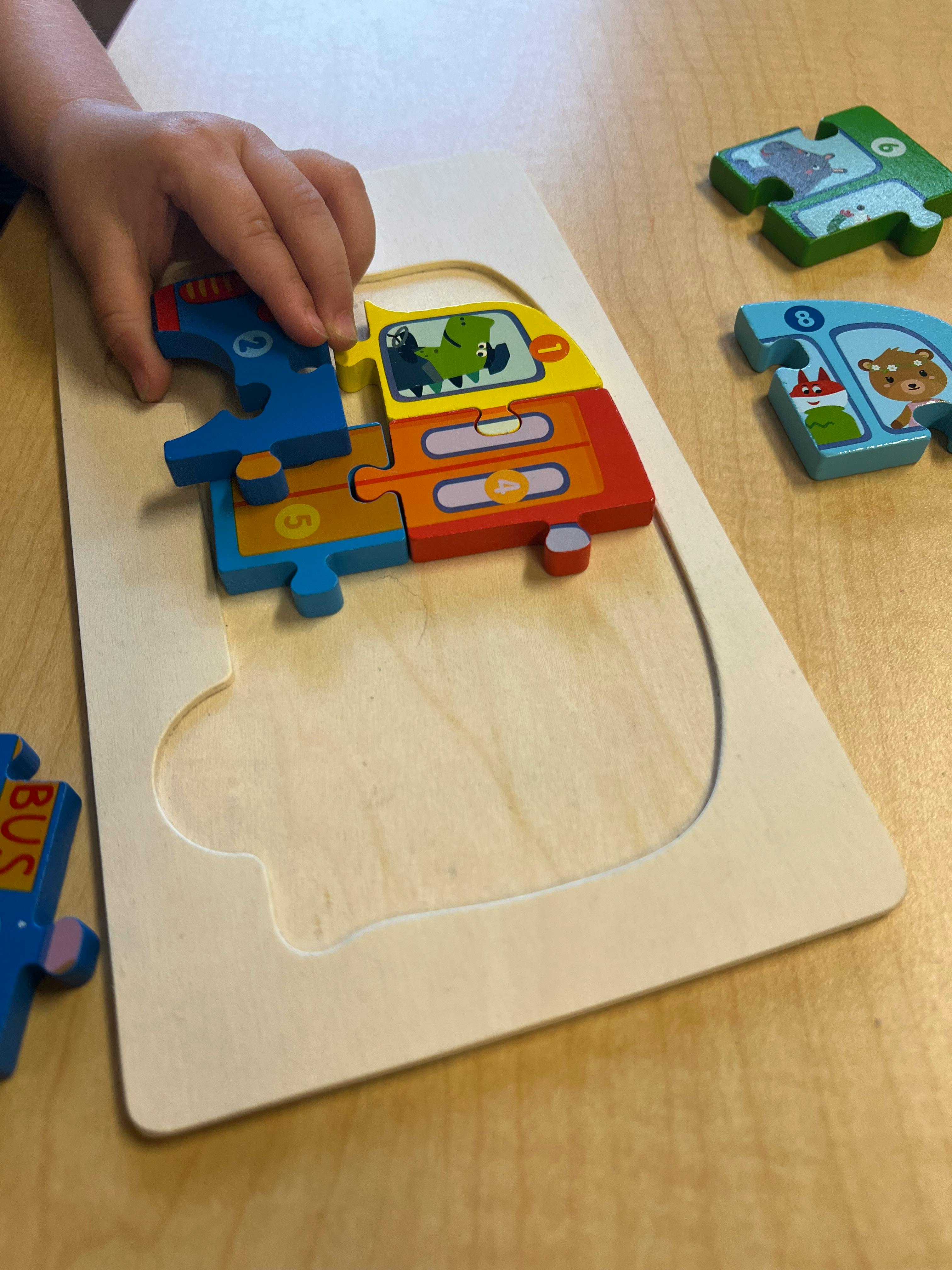 Child's hand placing a puzzle piece into a wooden bus puzzle