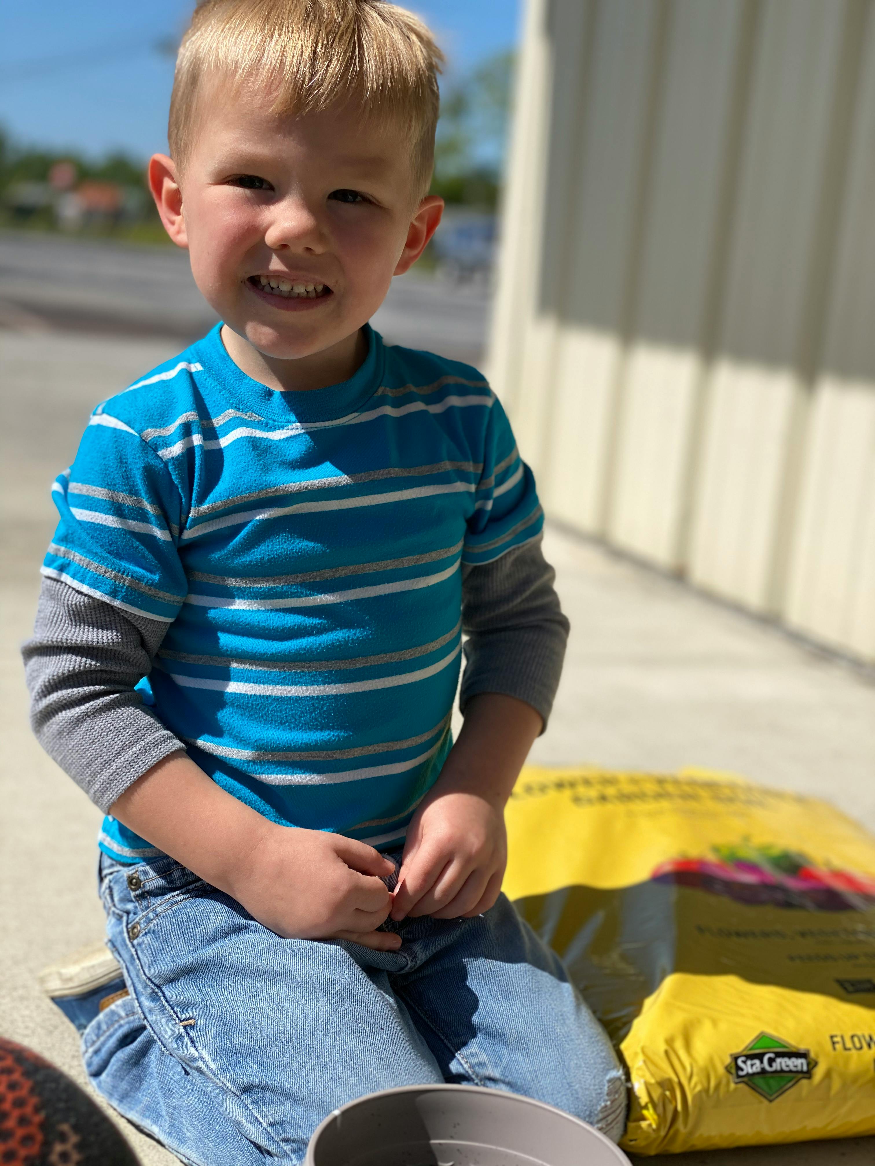 Child kneeling next to a bag of soil