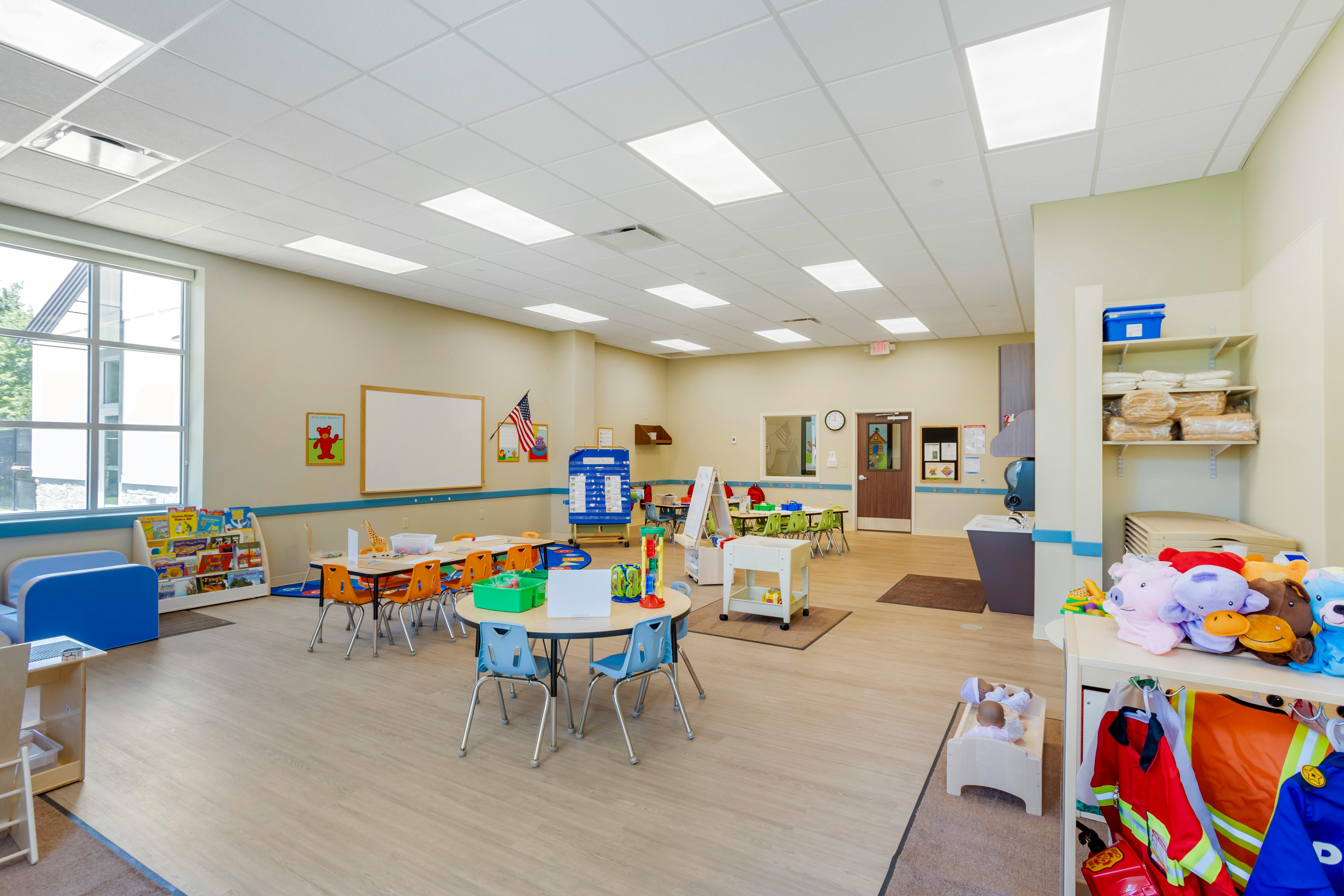 Classroom with multiple child-sized tables and chairs, toys, and learning materials