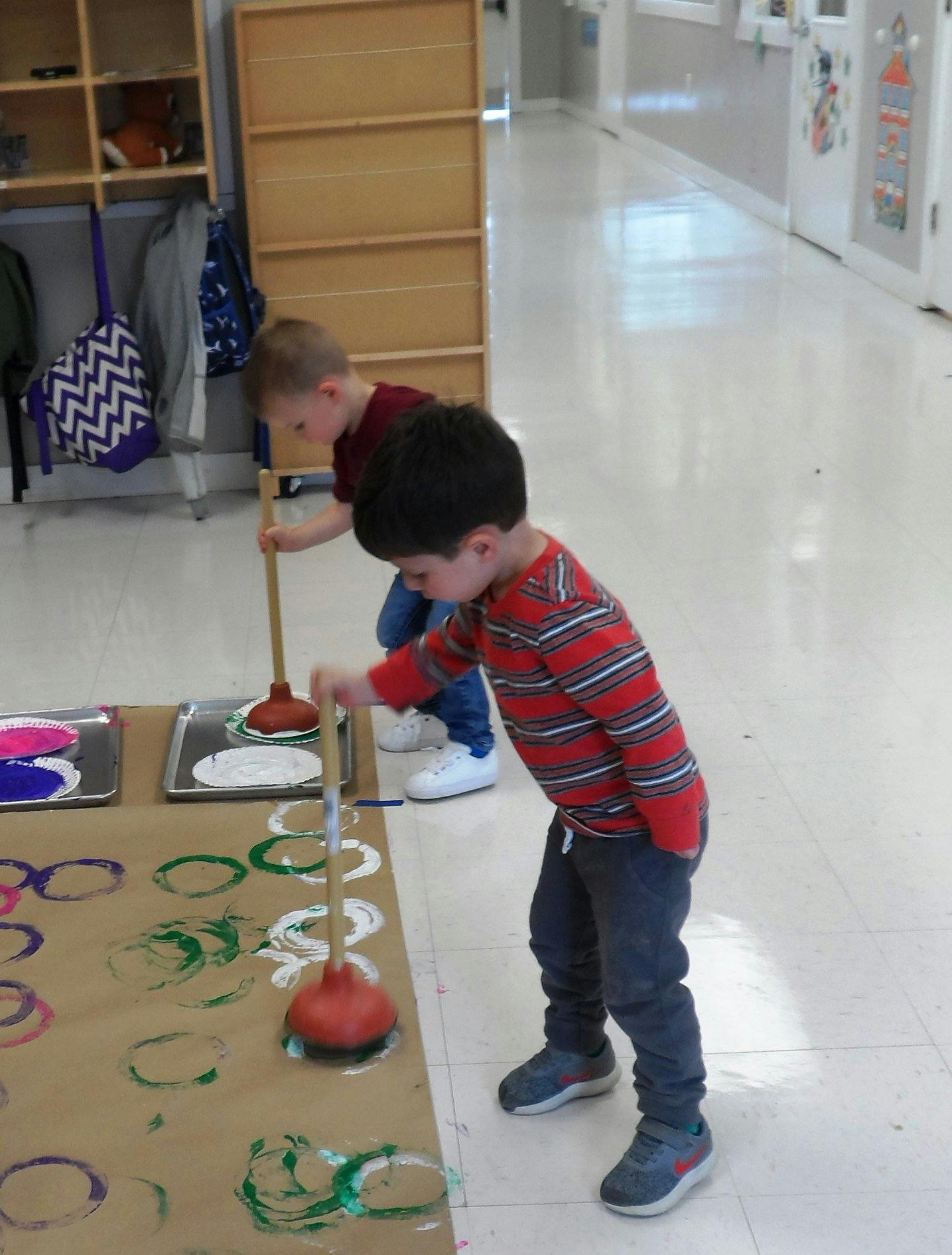 Two children using plungers to make paint prints on paper