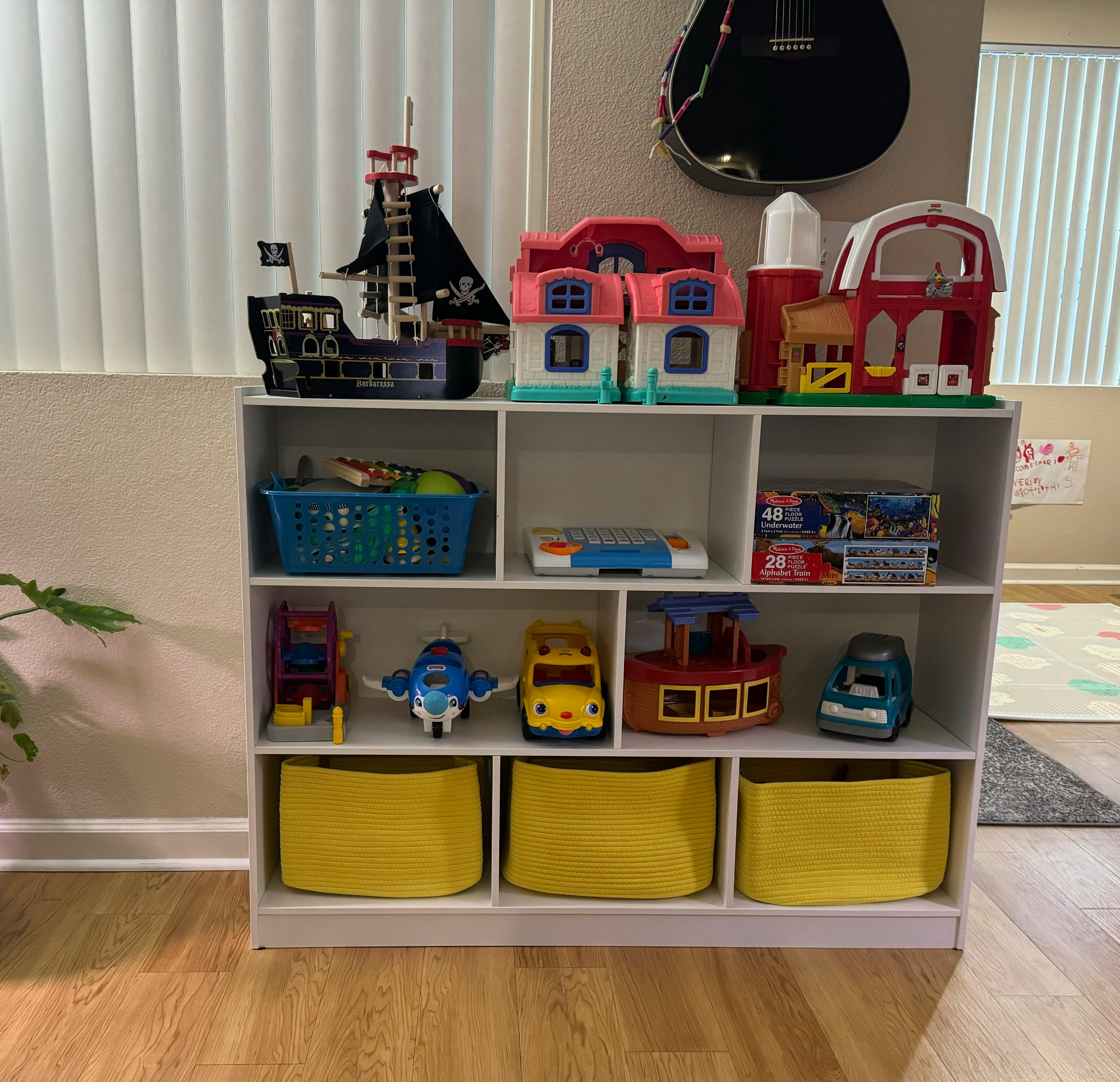 White shelving unit filled with various toys and yellow storage bins