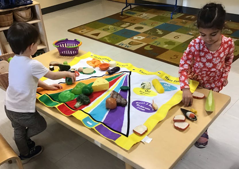 Two children playing with toy food on a colorful mat on a table