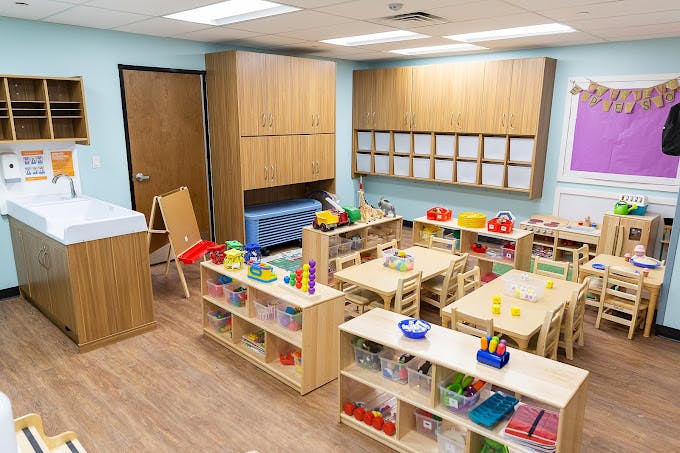 A classroom with small tables, chairs, shelves filled with toys, and a changing station