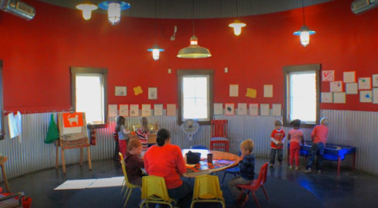 Adults and children in a classroom with red walls and windows