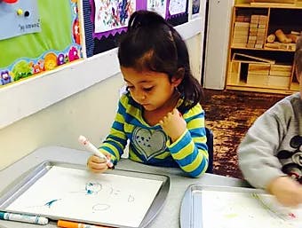 Child drawing on paper with a marker in a classroom