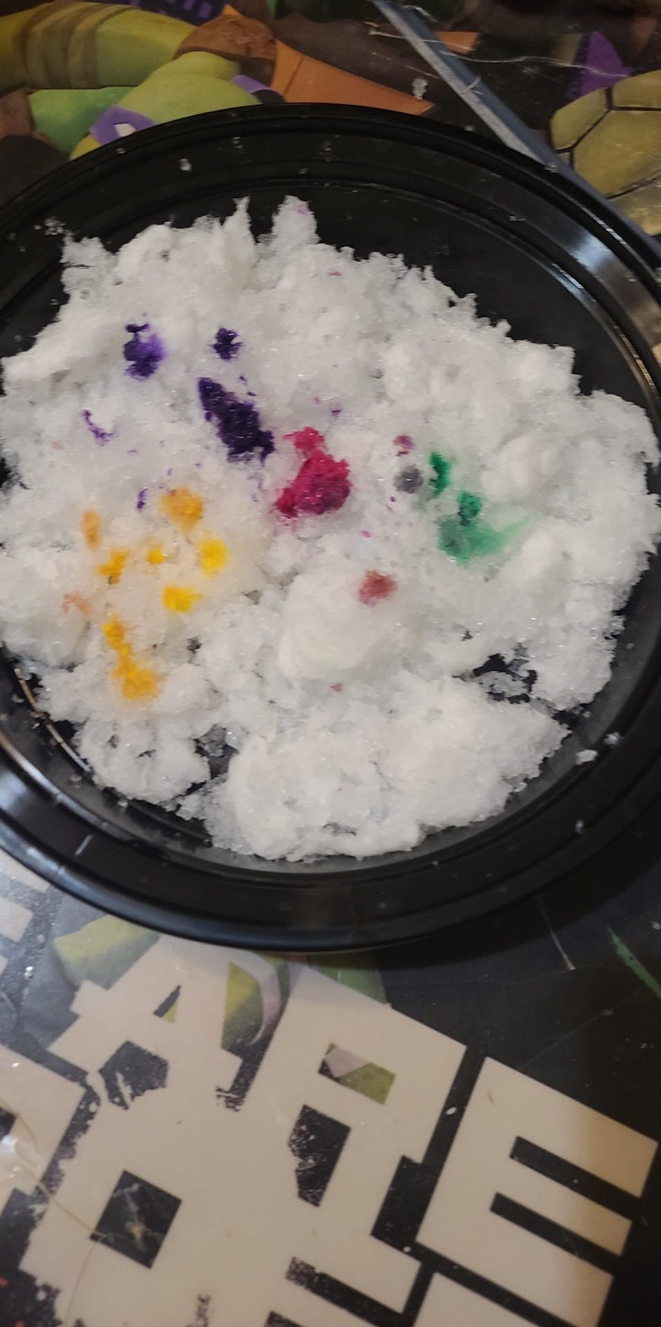 Snow cone with yellow, purple, pink, and green flavoring in a black bowl
