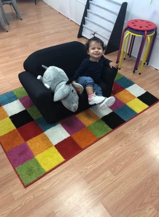 Child sitting in a black chair with a stuffed animal on a colorful rug