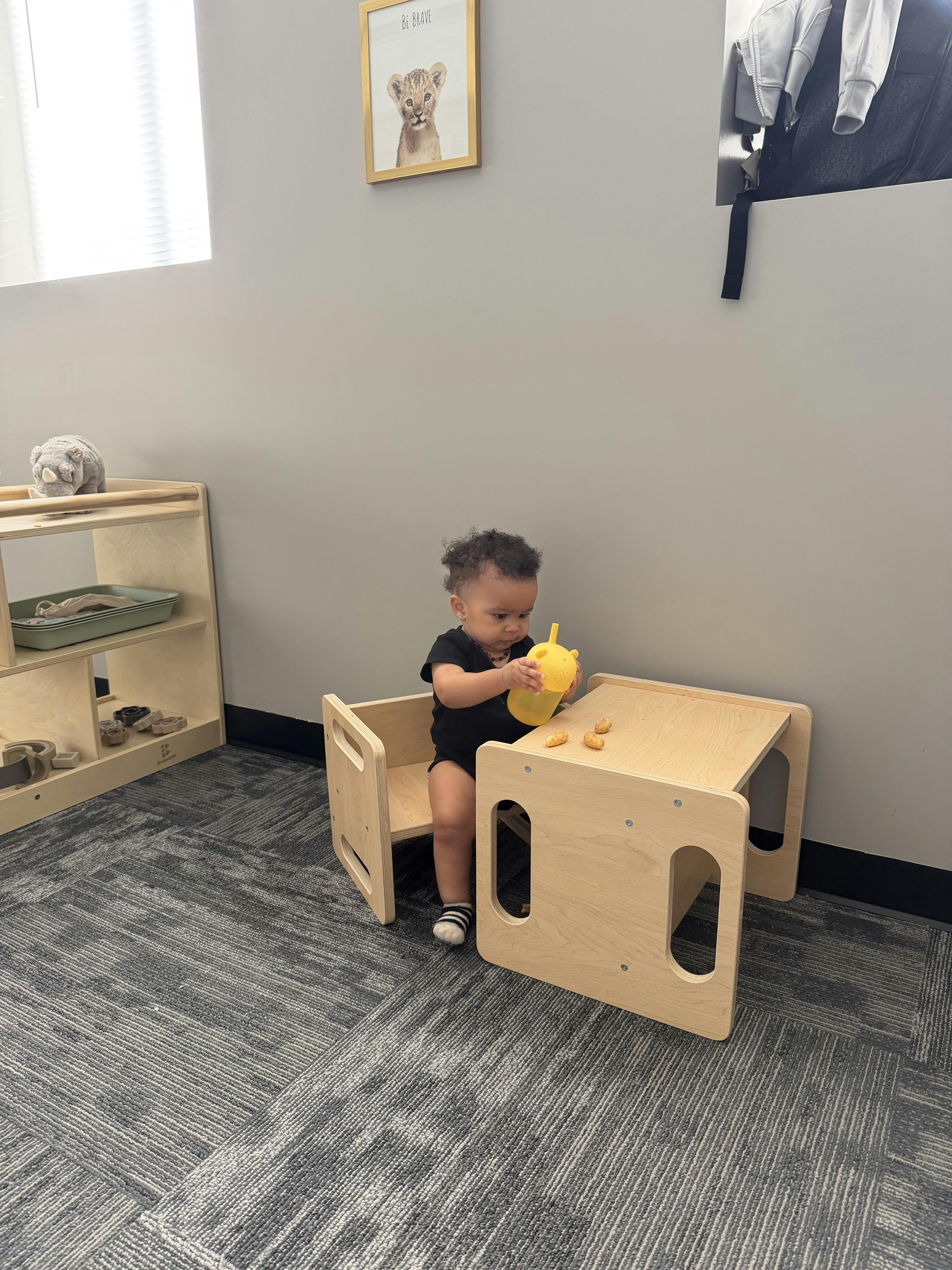 A child sitting at a small wooden table holding a cup