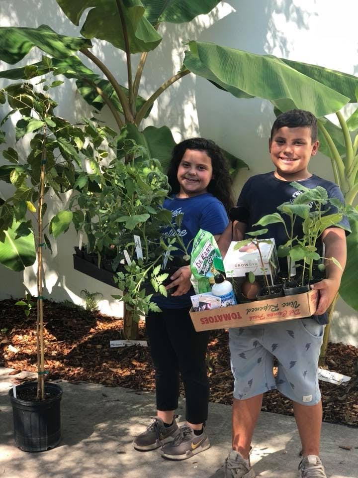 Two children holding trays of small plants and gardening supplies