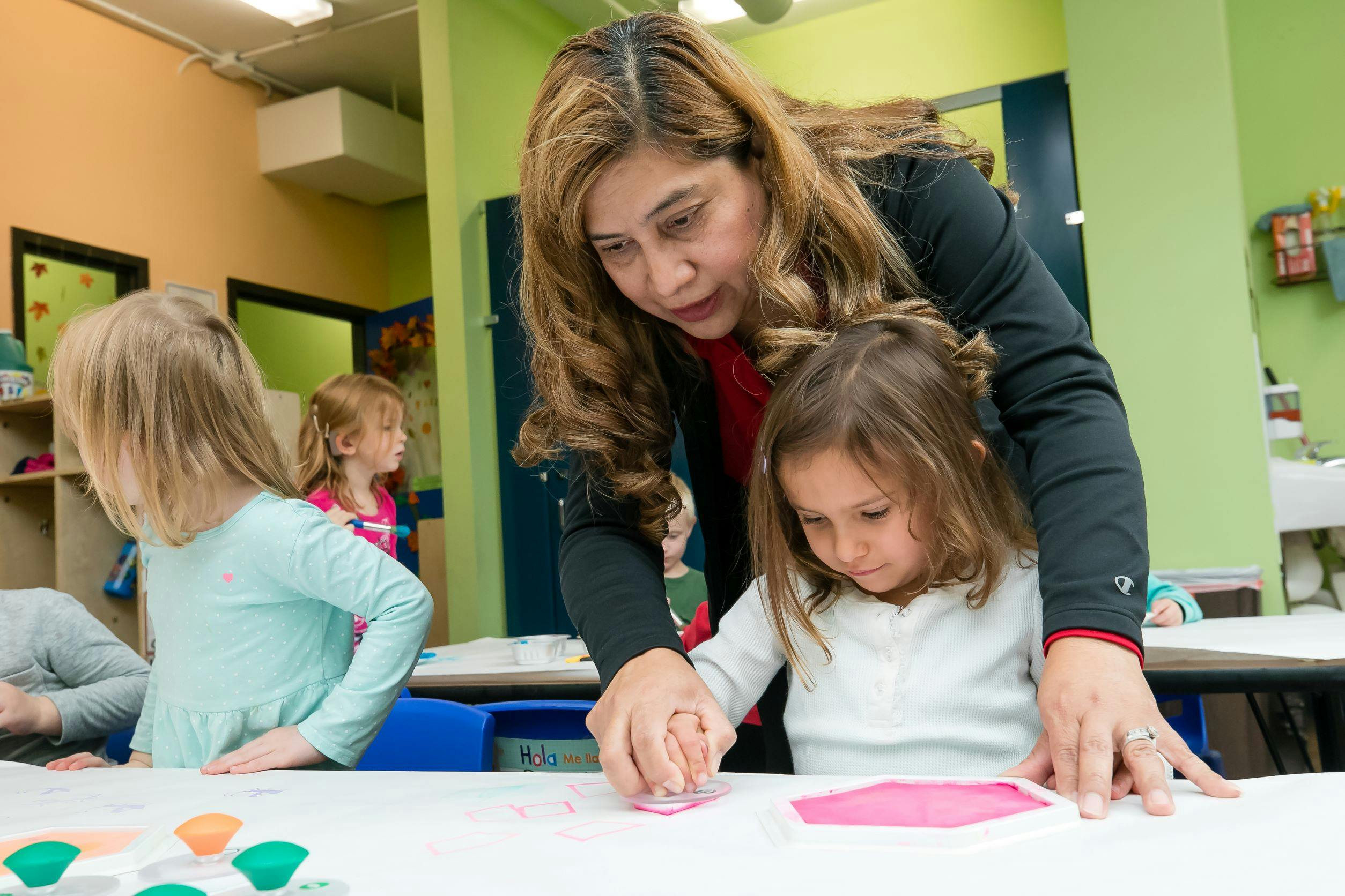 Adult helping a child with an art project in a classroom