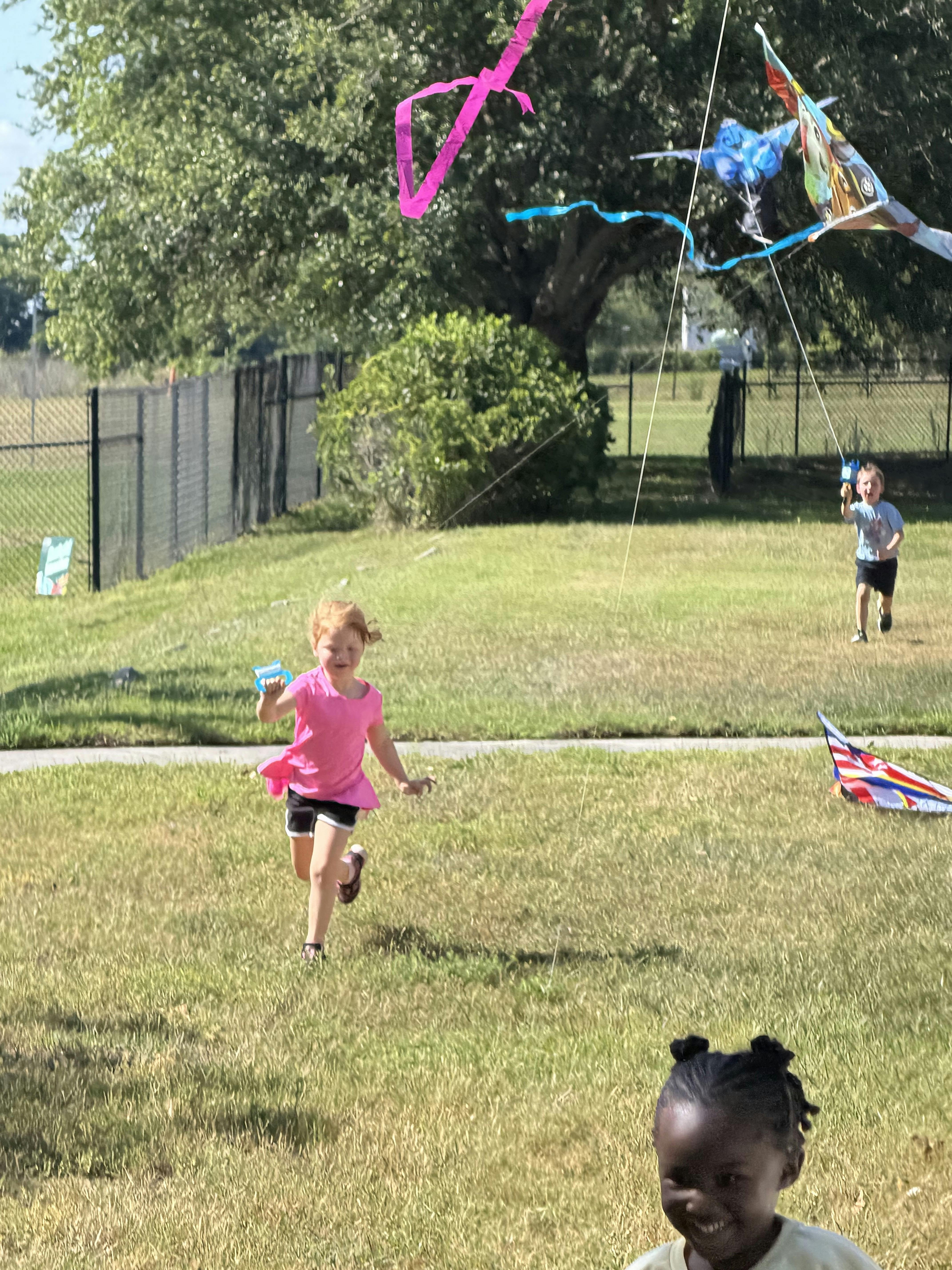 Three children flying kites in a grassy field