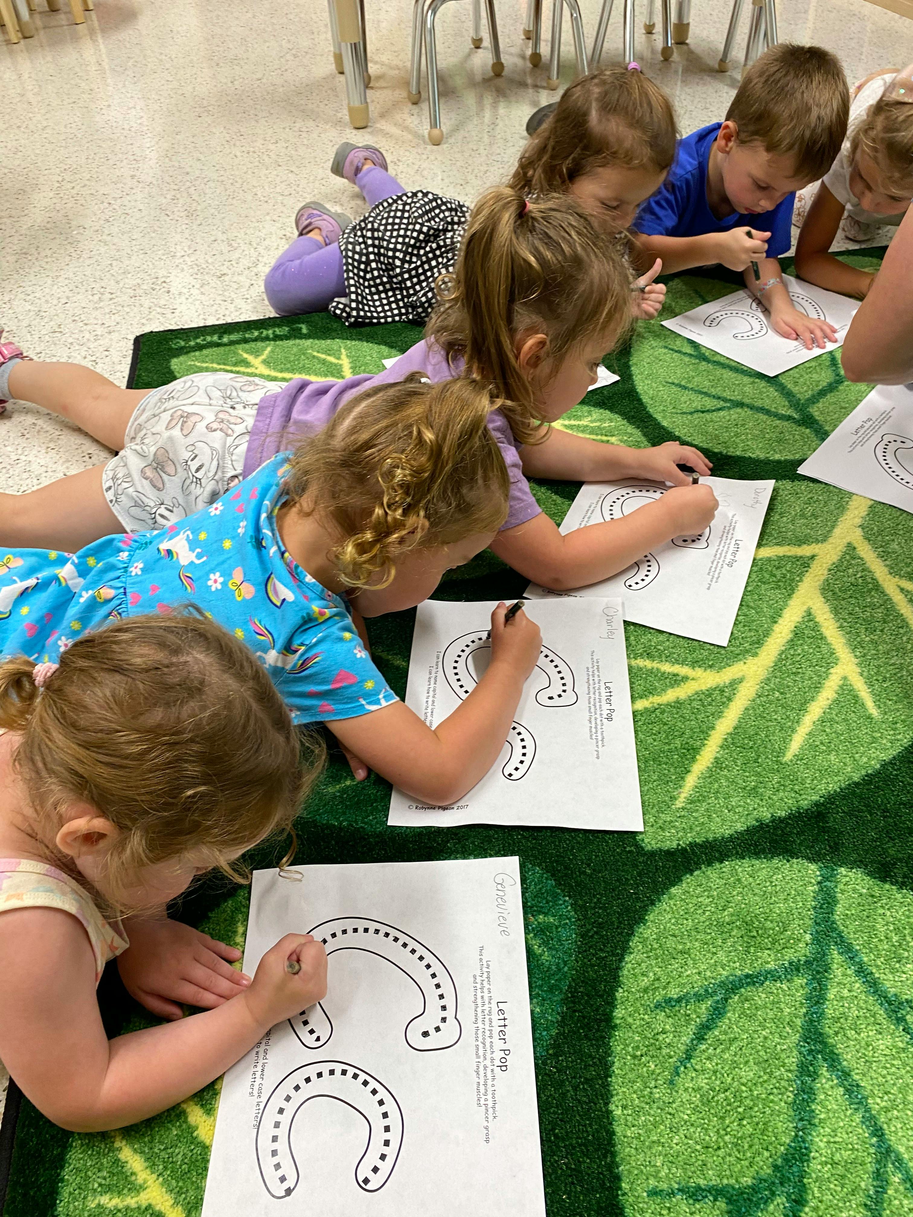Children lying on a rug practicing letter writing on worksheets