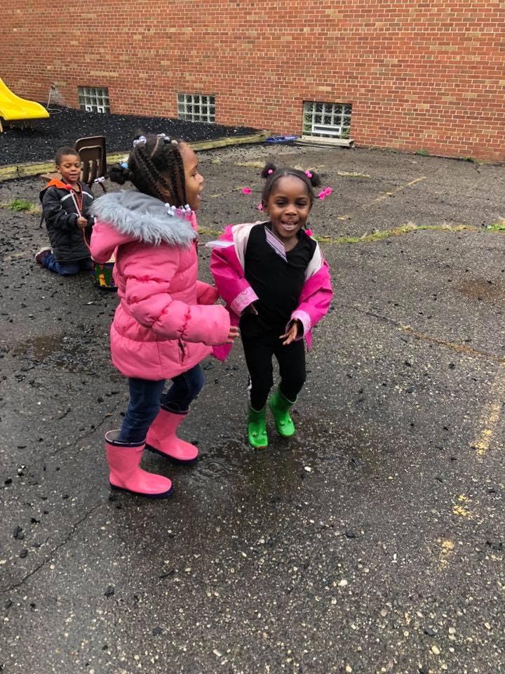 Two children in rain boots playing on wet pavement