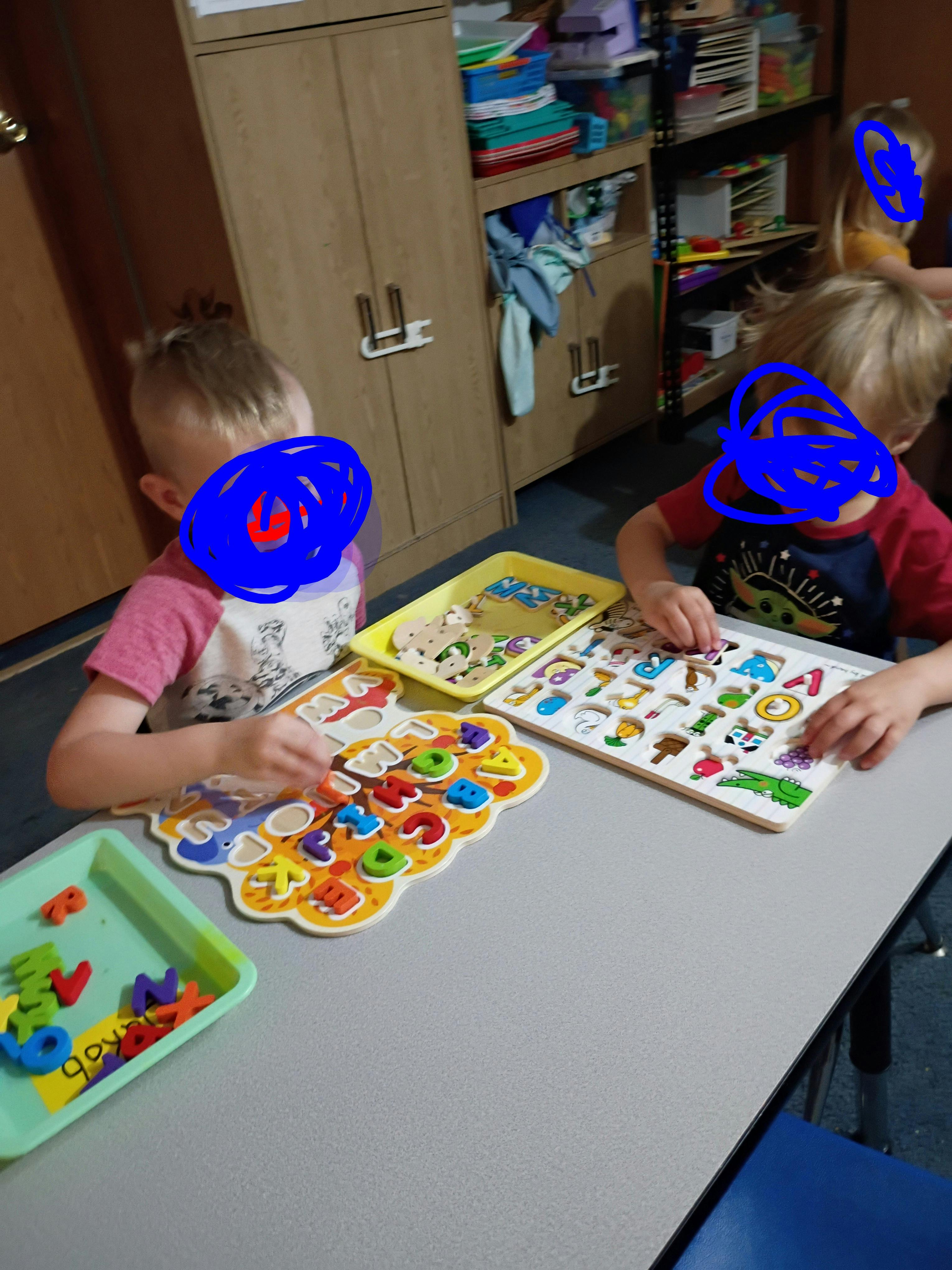 Two children sitting at a table playing with alphabet letter puzzles