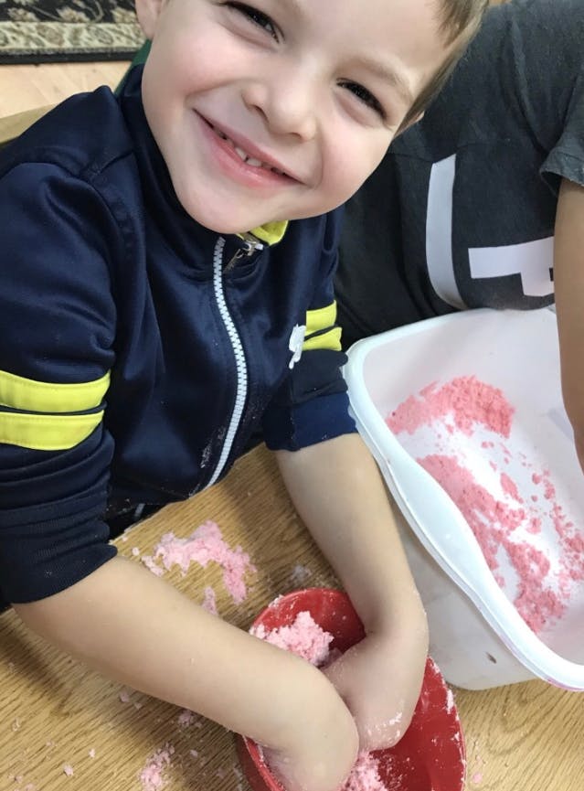 Child playing with pink dough in a red bowl