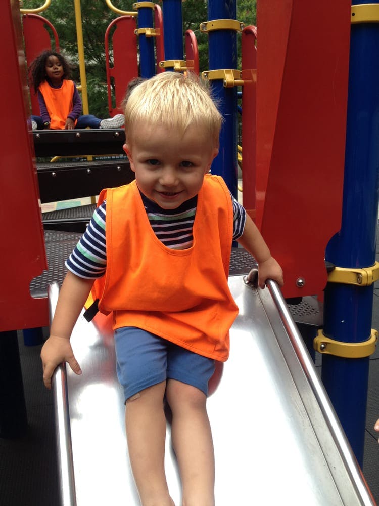 Child in orange vest on a playground slide