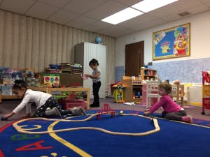 Three children playing with a toy train set on a rug in a room