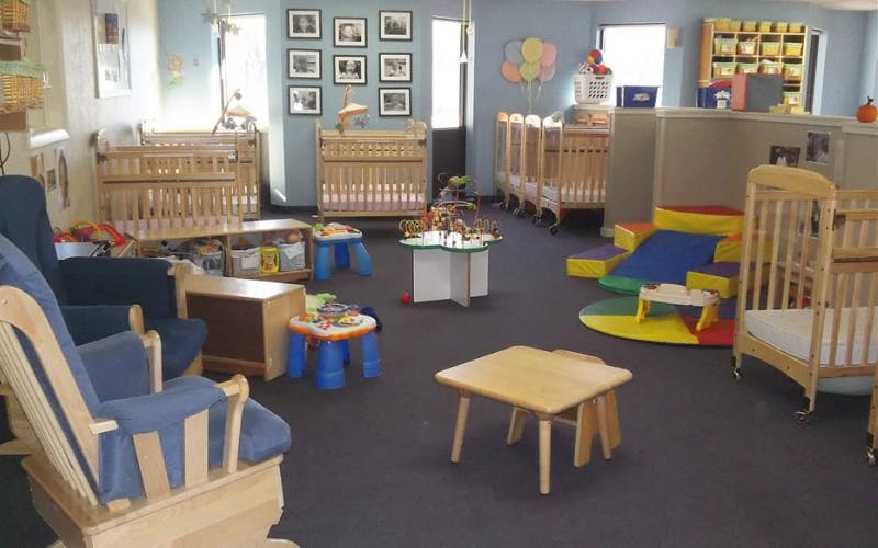 A brightly lit nursery room with multiple cribs, chairs, and play equipment